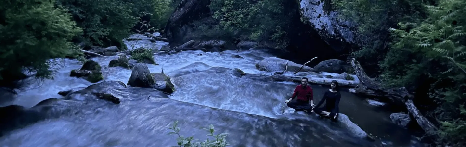 a couple doing yoga by a stream